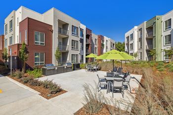 an outdoor patio with tables and umbrellas in front of an apartment building